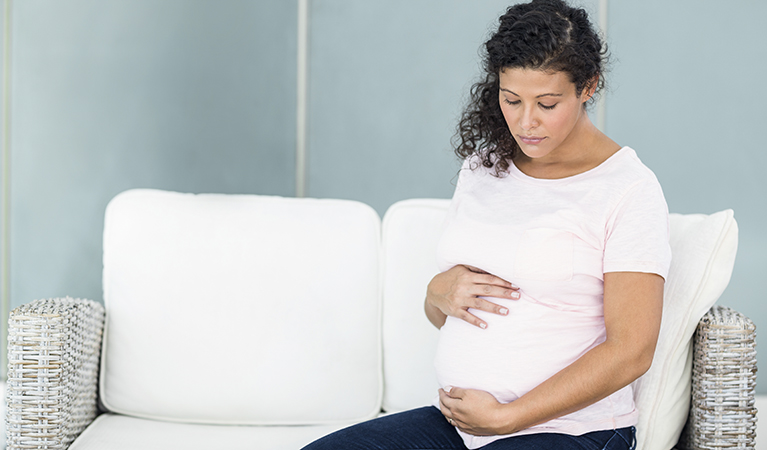 sad pregnant woman sitting on sofa against wall at home